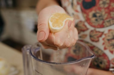 Mutfaktaki karıştırıcı bardağa limon suyu döken bir kadının elinden yakın bir fotoğraf..