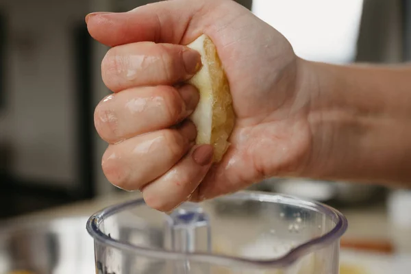 A close photo from the side of the strong hand of a woman who is crushing lemon juice by the hand into the blender cup in the kitchen.