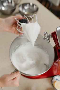 Mutfaktaki paslanmaz çelik bir çorba kasesinin yanında çırpıcı çırpıcısında krema sergileyen bir kadının yakın bir fotoğrafı..