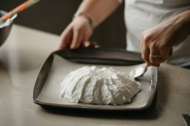 Tepside büyük bir krema şeklinde bir kaşık yapan genç bir kadının ellerinin yakın fotoğrafı. Bir kız lezzetli bir limonlu pasta pişirmeye hazırlanıyor..