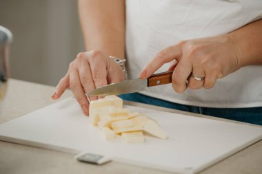 Kesici bir bıçakla taze çiftlik tereyağını kesen genç bir kadının yakın bir fotoğrafı..