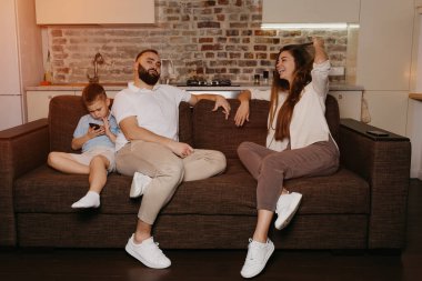 Oğlu akşamları cep telefonuyla oyun oynarken anne ve baba kanepede TV 'nin keyfini çıkarıyorlar. Evde akrabalar.