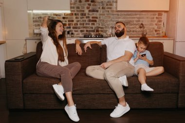 Oğlu akşamları cep telefonuyla oyun oynarken anne ve baba kanepede TV 'nin keyfini çıkarıyorlar. Evde akrabalar.