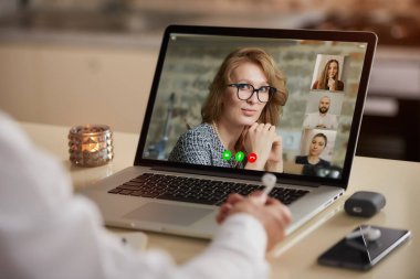 Bir adamın omzunun üzerinden yapılan çevrimiçi bir toplantı sırasında telekomünikasyon uygulamasının laptop ekran görüntüsü. İş arkadaşlarıyla bir video konferansında kulaklık tutan bir çalışanın arka görüntüsü.