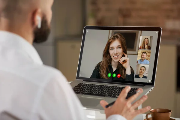 Kulaklıklı kel bir erkek çalışanın evde bir video konferansı sırasında el kol hareketi yapması. Bir adamın omzunun üzerinden yapılan çevrimiçi bir toplantının telekomünikasyon uygulamasının laptop ekran görüntüsü