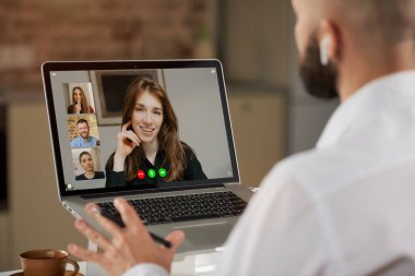 Kulaklıklı kel bir erkek çalışanın evde bir video konferansı sırasında el kol hareketi yapması. Bir adamın omzunun üzerinden yapılan çevrimiçi bir toplantının telekomünikasyon uygulamasının laptop ekran görüntüsü