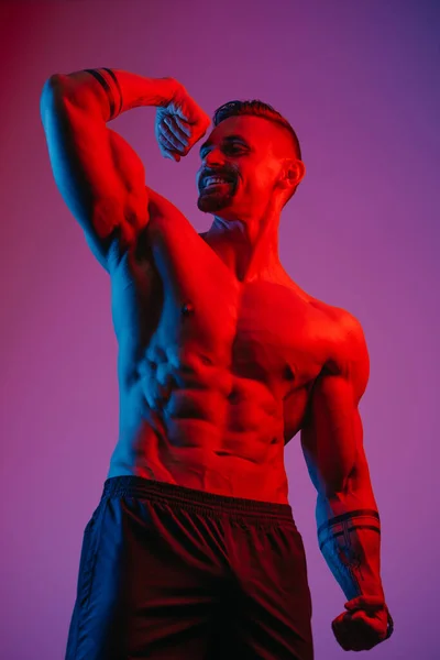 Uśmiechnięty Kulturysta Brodą Pozuje Elastycznym Bicepsem Pod Niebieskim Czerwonym Światłem — Zdjęcie stockowe