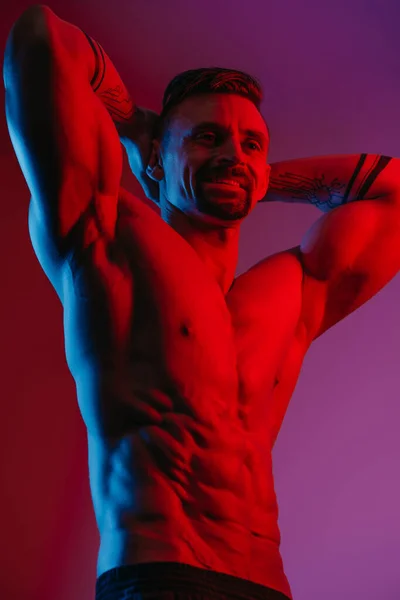 一个留着胡子的肌肉男在蓝光和红光下展示前腹姿势的侧影 一个运动员在摆姿势 运动后穿短裤的运动员 — 图库照片