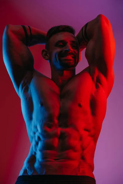 一个留着胡子的肌肉发达的男人正站在蓝光和红光下 一个运动员正在展示前腹姿势 运动后穿短裤的运动员 — 图库照片
