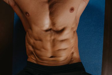 Mavi yoga minderinde mekik çekerken vücut geliştiren birinin karın kaslarının üstünden bir fotoğraf..