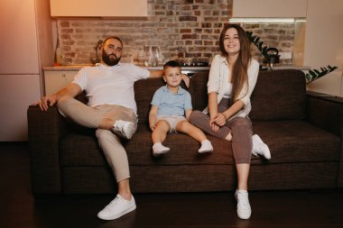 Baba, oğul ve anne evdeki kanepede televizyon izliyorlar. Aile akşamın tadını çıkarıyor. Memleketteki akrabalar. Uzun saçlı genç bir anne gülümsüyor..