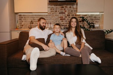 Baba, oğul ve anne evdeki kanepede TV ile izliyorlar. Aile evde mutlu bir akşamın tadını çıkarıyor. Baba, oğluna ve karısına bakıyor..