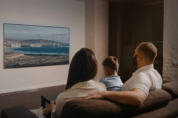 Bir baba, bir oğul ve kanepenin üzerinde geniş ekran bir televizyondan film izleyen genç bir annenin arkasından çekilmiş bir fotoğraf. Aile akşamları evde videonun keyfini çıkarıyor..