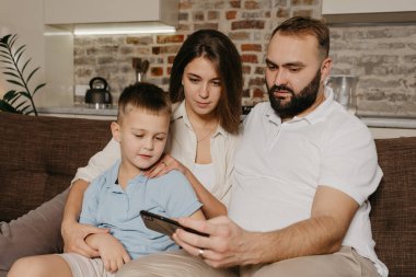 Bir baba, bir oğul ve bir anne kanepede video izliyorlar. Bir koca, akşam evde gülen bir çocuk ve eşe akıllı telefondan programı gösteriyor..