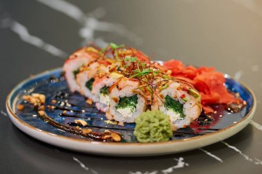 Chuka Wakame deniz yosunu, Philadelphia peyniri ve soslu, fıstıklı, zencefilli ve wasabi 'li karidesli suşi rulolarının yakın plan fotoğrafı. Siyah taş masa..