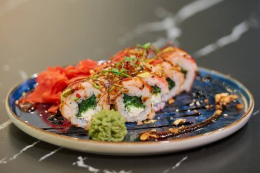 Chuka Wakame deniz yosunu, Philadelphia peyniri ve soslu, fıstıklı, zencefilli ve wasabi 'li karidesli suşi rulolarının yakın plan fotoğrafı. Siyah taş masa..