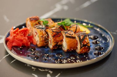 Somon, Philadelphia peynirli suşi ruloları ve soslu, susamlı, kumkuat, wasabi ve yapraklı mavi seramik tabakta ton balığı. Siyah taş masa..