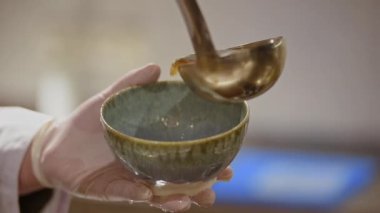 Mavi seramik kâsenin yakın plan bir videosunda erkek bir aşçı mutfağa geleneksel Japon çorbası döküyor..