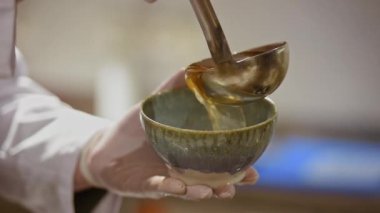 Mavi seramik kasede tek kullanımlık eldivenli bir erkek aşçının mutfağa geleneksel Japon çorbası döktüğü bir video..