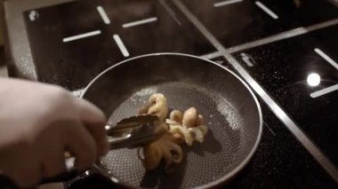 İçinde kaynar yağ olan bir tavada, elinde pens olan bir aşçı mutfakta ahtapot kızartıyordu..