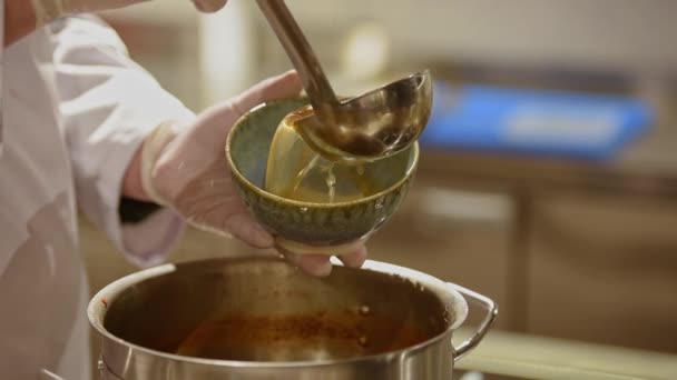 日本の伝統的なスープを注ぐ白い使い捨て手袋で男性料理人の手のクローズアップビデオキッチンの青いセラミックボウルにラーメン — ストック動画