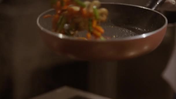 フライパンに野菜を入れ キッチンの使い捨て手袋で手で料理を投げ上げていく様子を密着映像で撮影 皿の上の蒸気パフ — ストック動画