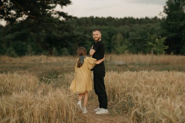 Sakallı genç bir çiftçinin kızı gün batımında ormandaki buğday tarlasının kenarında ona sarılıyor. Mutlu baba ve çocuk.