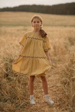 Gün batımında çavdar tarlasının ortasında dans eden, elbiseli mutlu genç bir kızın tam boy portresi..