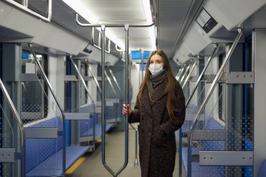 Coronavirus 'un yayılmasını önlemek için tıbbi maske takan bir kadın modern bir metro vagonunda tırabzanı tutuyor. Cerrahi maskeli bir kız metroda sosyal mesafeyi koruyor..