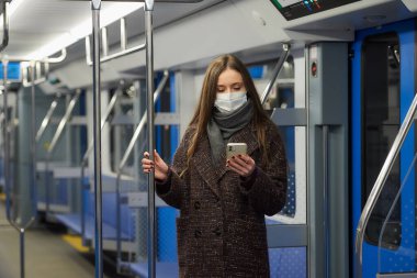 Coronavirus 'un yayılmasını önlemek için tıbbi maske takan bir kadın boş bir metro vagonunda akıllı telefon kullanıyor. Cerrahi maskeli bir kız trende cep telefonuyla haberlere çıkıyor..