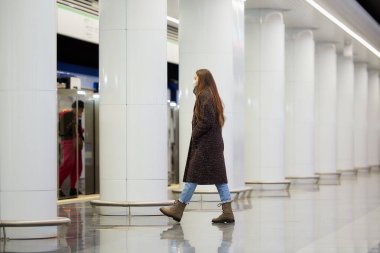 Metroya binecek olan Coronavirus 'un yayılmasını önlemek için tıbbi maske takan bir kadının tam boy fotoğrafı. Cerrahi maskeli bir kız metro istasyonunda sosyal mesafeyi koruyor..
