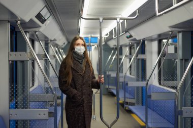 Coronavirus 'un yayılmasını önlemek için tıbbi maske takan bir kadın modern bir metro vagonunda tırabzanı tutuyor. Cerrahi maskeli bir kız metroda sosyal mesafeyi koruyor..