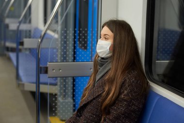 Modern bir metro vagonunda tek başına oturan Coronavirus 'un yayılmasını önlemek için tıbbi maske takan bir kadının yakın bir fotoğrafı. Cerrahi maskeli bir kız metroda sosyal mesafeyi koruyor..