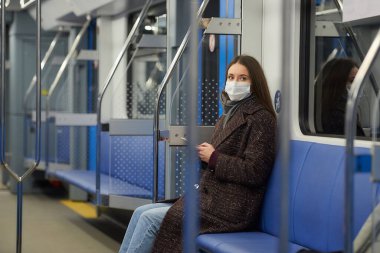 Coronavirus 'un yayılmasını önlemek için tıbbi maske takan bir kadın modern bir metro vagonunda yan yana oturuyor. COVID-19 'a karşı cerrahi maske takan bir kız metro trenine biniyor..
