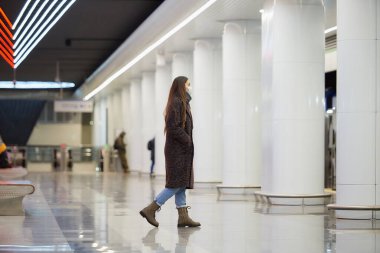 Metroya binecek olan Coronavirus 'un yayılmasını önlemek için tıbbi maske takan bir bayanın tam boy fotoğrafı. Cerrahi maskeli bir kız metro istasyonunda sosyal mesafeyi koruyor..
