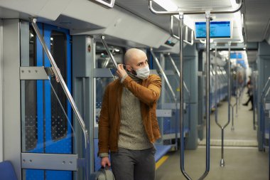Sakallı bir adam metroda koronavirüsün yayılmasını önlemek için tıbbi maske takıyor. COVID-19 'a karşı cerrahi maskeli kel bir adam trende sosyal mesafeyi koruyor..