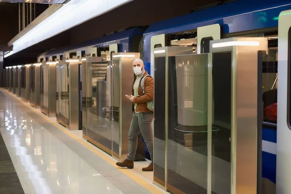 코로나 바이러스가 퍼지지 않도록 의료용 마스크를 지하철 차량을 떠나면서 스마트폰을 — 스톡 사진