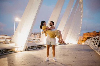 Sakallı bir adam Valencia 'daki beyaz bir köprüde sarı elbiseli kızını kollarında tutuyor. Sıcak bir akşamda bir çift turist uzun bir randevuya çıktı..