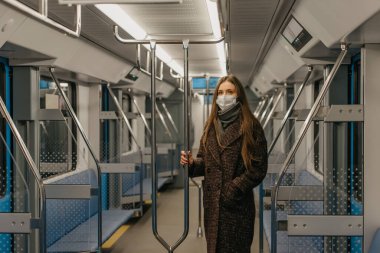 Coronavirus 'un yayılmasını önlemek için tıbbi maske takan bir kadın modern bir metro vagonunda tırabzanı tutuyor. Cerrahi maskeli bir kız metroda sosyal mesafeyi koruyor..