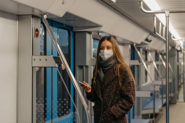 Coronavirus 'un yayılmasını önlemek için tıbbi maske takan bir kadın kapıların yanında duruyor ve boş bir metro vagonunda yan tarafa bakıyor. Cerrahi maskeli bir kız metro trenine biniyor..