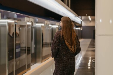 Coronavirus 'un yayılmasını önlemek için tıbbi maske takan bir kadın modern metro vagonuna gidiyor. Cerrahi maskeli bir kız metro istasyonunda sosyal mesafeyi koruyor..