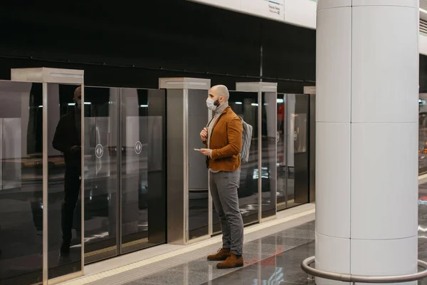 얼굴에 마스크를 남성의 지하철 승강장에서 열차를 기다리는 스마트폰을 외과용 마스크를 — 스톡 사진