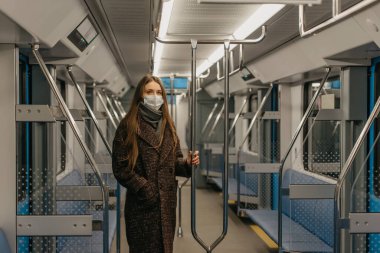 Coronavirus 'un yayılmasını önlemek için tıbbi maske takan bir kadın modern bir metro vagonunda tırabzanı tutuyor. Cerrahi maskeli bir kız metroda sosyal mesafeyi koruyor..