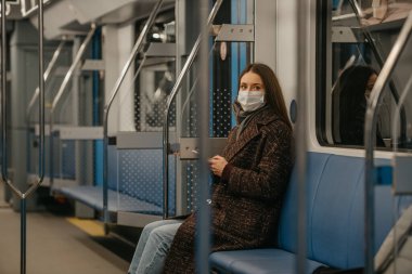 Coronavirus 'un yayılmasını önlemek için tıbbi maske takan bir kadın modern bir metro vagonunda yan yana oturuyor. COVID-19 'a karşı cerrahi maske takan bir kız metro trenine biniyor..