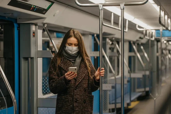 Coronavirus 'un yayılmasını önlemek için tıbbi maske takan bir kadın boş bir metro vagonunda akıllı telefon kullanıyor. Cerrahi maskeli bir kız trende cep telefonuyla haberlere çıkıyor..