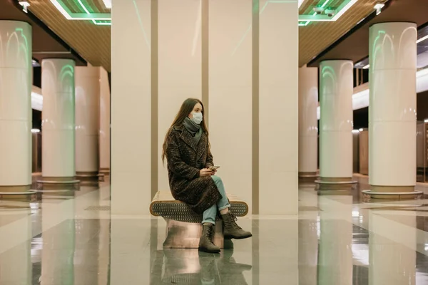 코로나 바이러스가 퍼지지 않도록 의료용 마스크를 외로운 지하철역 플랫폼에서 스마트폰을 — 스톡 사진