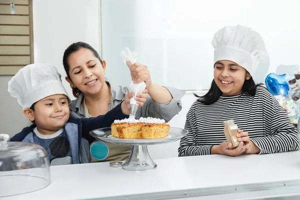 Latina mom decorating a cake with her kids - Hispanic kids having fun in the kitchen with their mom - pastry kids