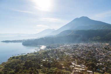 Sabahları Atitlan Gölü 'ndeki San Juan la Laguna' nın havadan görünüşü - Dağlarla çevrili küçük göl kenti ve güneş ışığı olan volkanlar.
