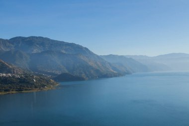 Sabahleyin Guatemala 'daki Atitlan Gölü, San Juan la Laguna' nın manzarasından görüldü. Etrafı gün ışığıyla çevrili dağlarla çevrili bir göl manzarası.
