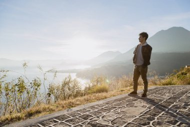 Genç gezgin dağın tepesinde Atitlan Gölü 'nde güneşin doğuşunu seyrediyor. İspanyol genç adam volkanlar ve dağlarla güneşin doğuşunu seyrediyor.